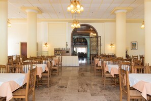 Μια μεγάλη τραπεζαρία με πολλά τραπέζια και καρέκλες, ένα πολυέλαιο και μια κεντρική αψίδα.