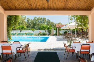 Zona de piscina exterior con mesas y sillas, rodeada de vegetación y un cielo despejado.