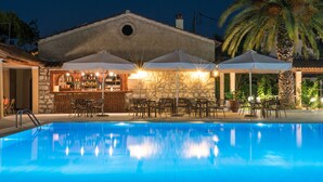 A swimming pool with a bar area, outdoor seating, and a stone building with a circular window. - Sunset Hotel Corfu (Corfu)