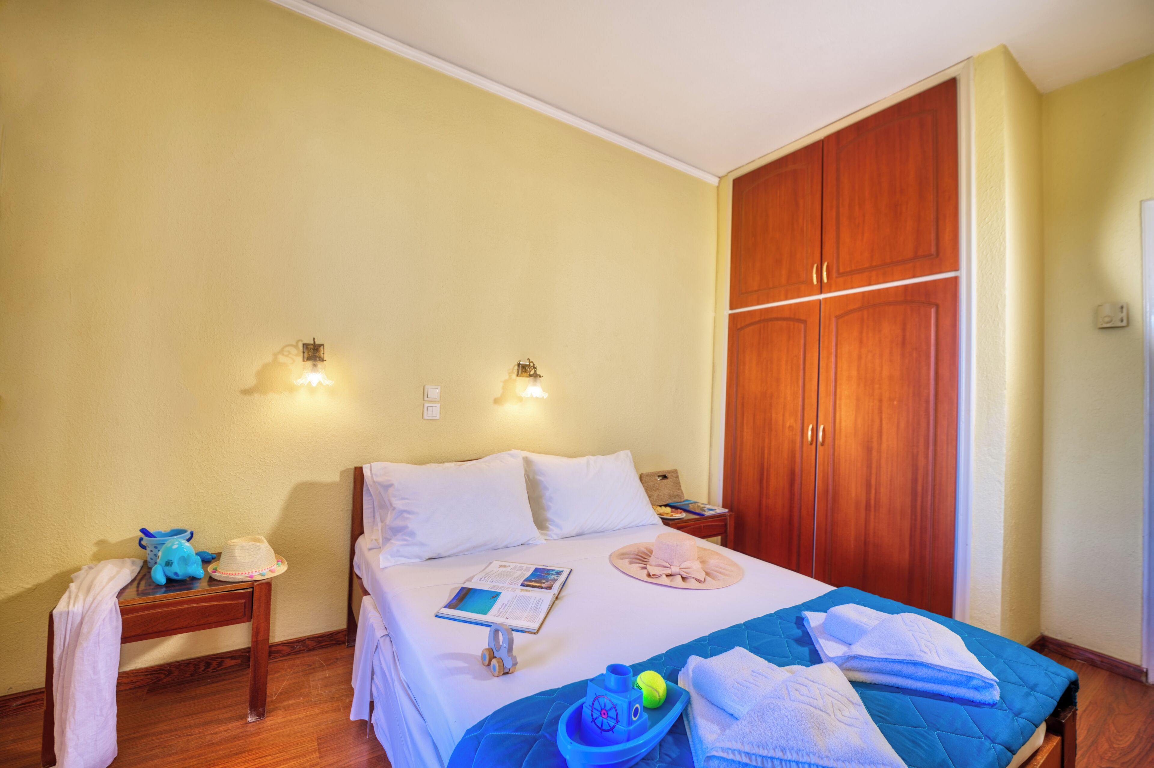 A hotel room with a bed, wooden wardrobe, bedside tables, and wall-mounted lights.