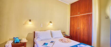 Una habitación de hotel con cama, armario de madera, mesitas de noche e iluminación en la pared.