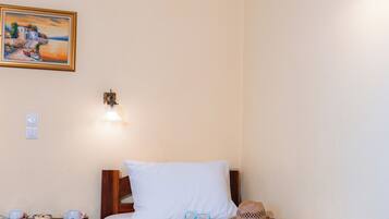 Una habitación de hotel con una cama, una mesita de noche, una lámpara, un cuadro y un sombrero sobre la cama.