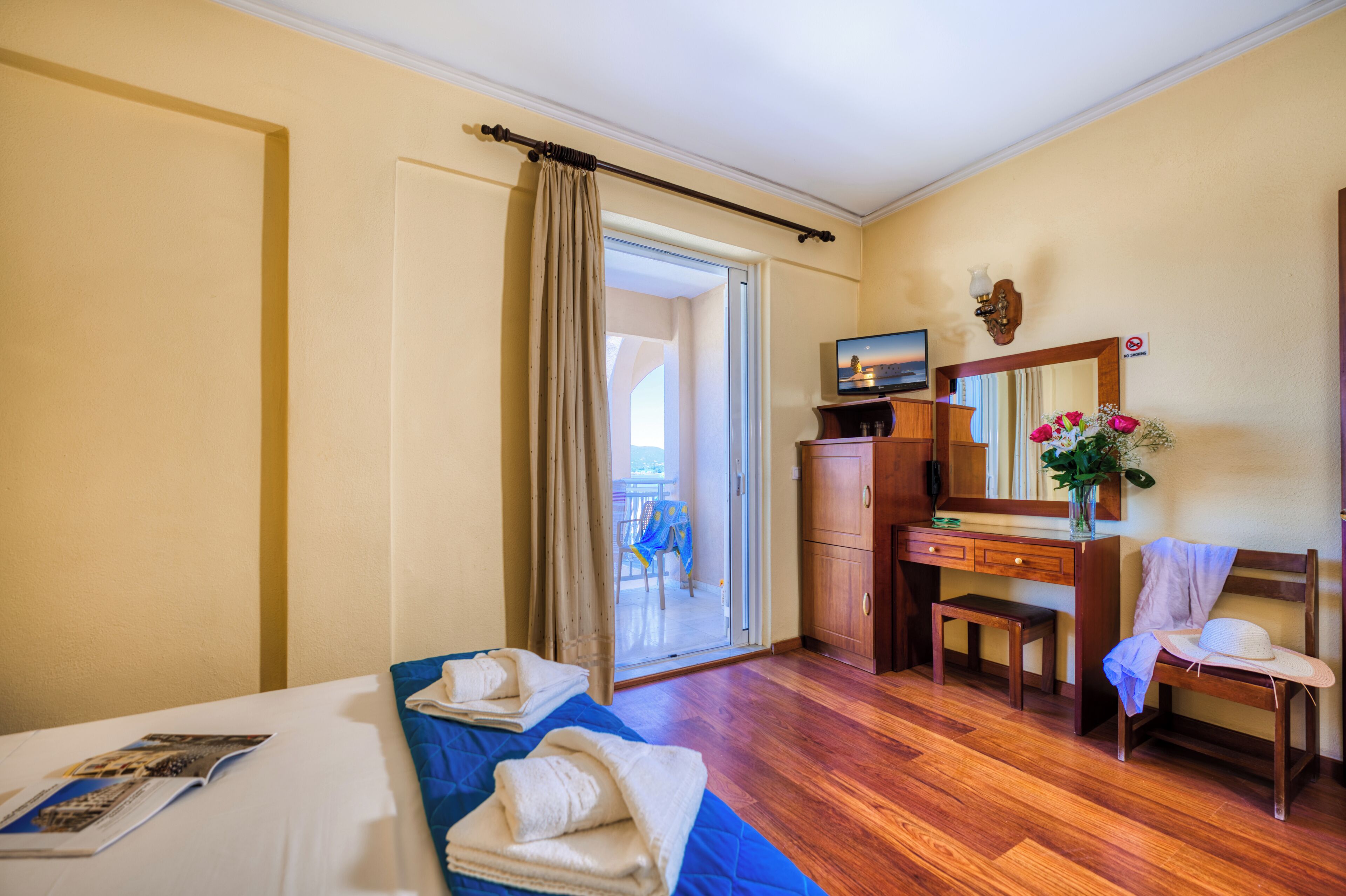 Habitación de hotel con cama, escritorio, silla, mesita, espejo y vistas al exterior.