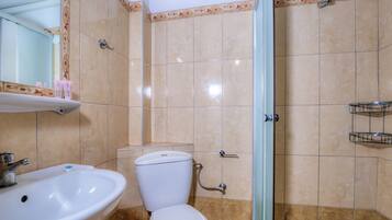 A bathroom with a toilet, sink, shower, and tiled walls.