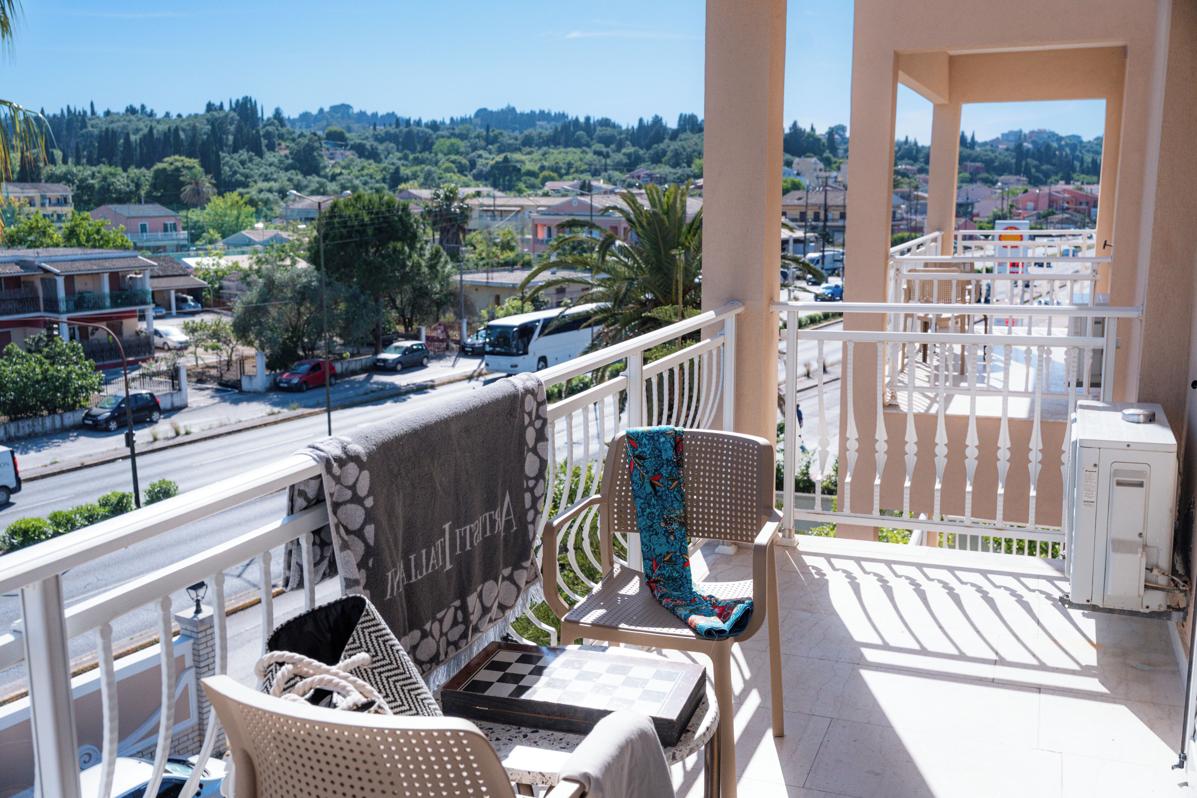 A balcony with a view of a street, a chair, a table with a chessboard, and a towel with 'ITALIA' on it.