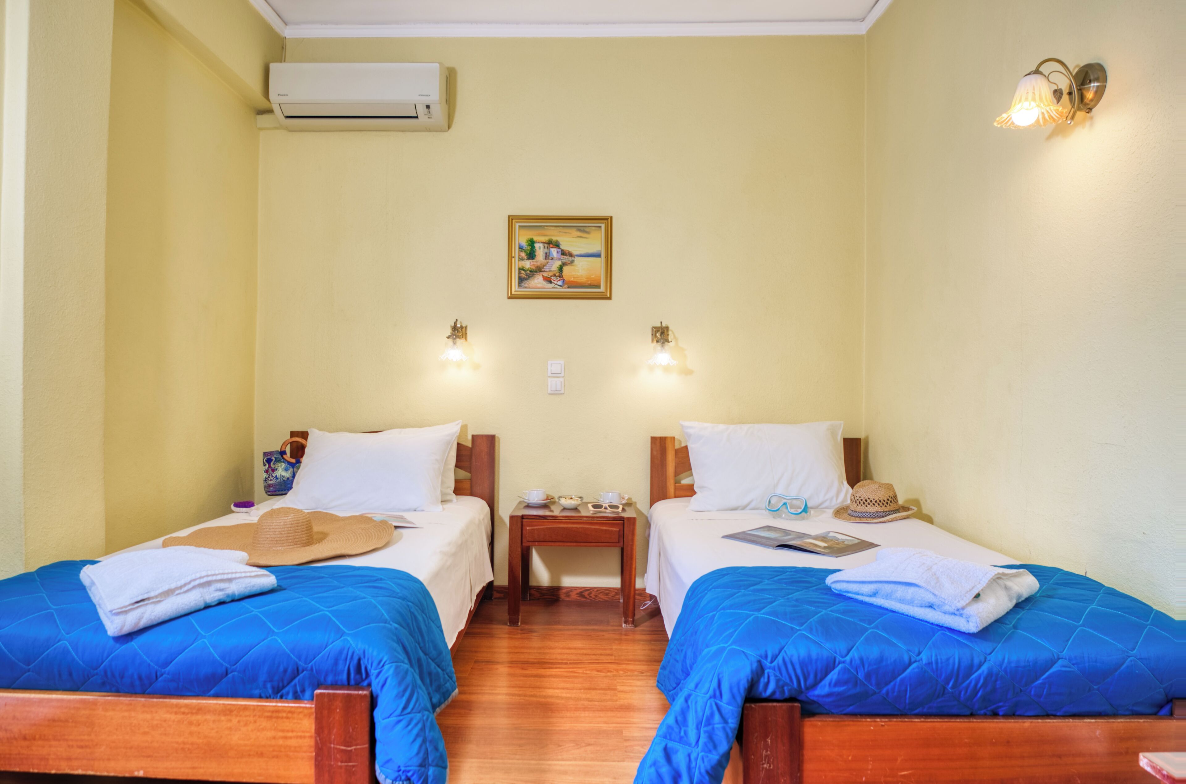 A hotel room with two beds, a nightstand, a wall-mounted air conditioner, and a painting.