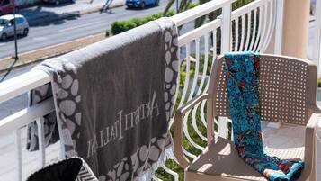 A balcony with a chessboard, a chair with a patterned cushion, and a view of a street with cars and palm trees.