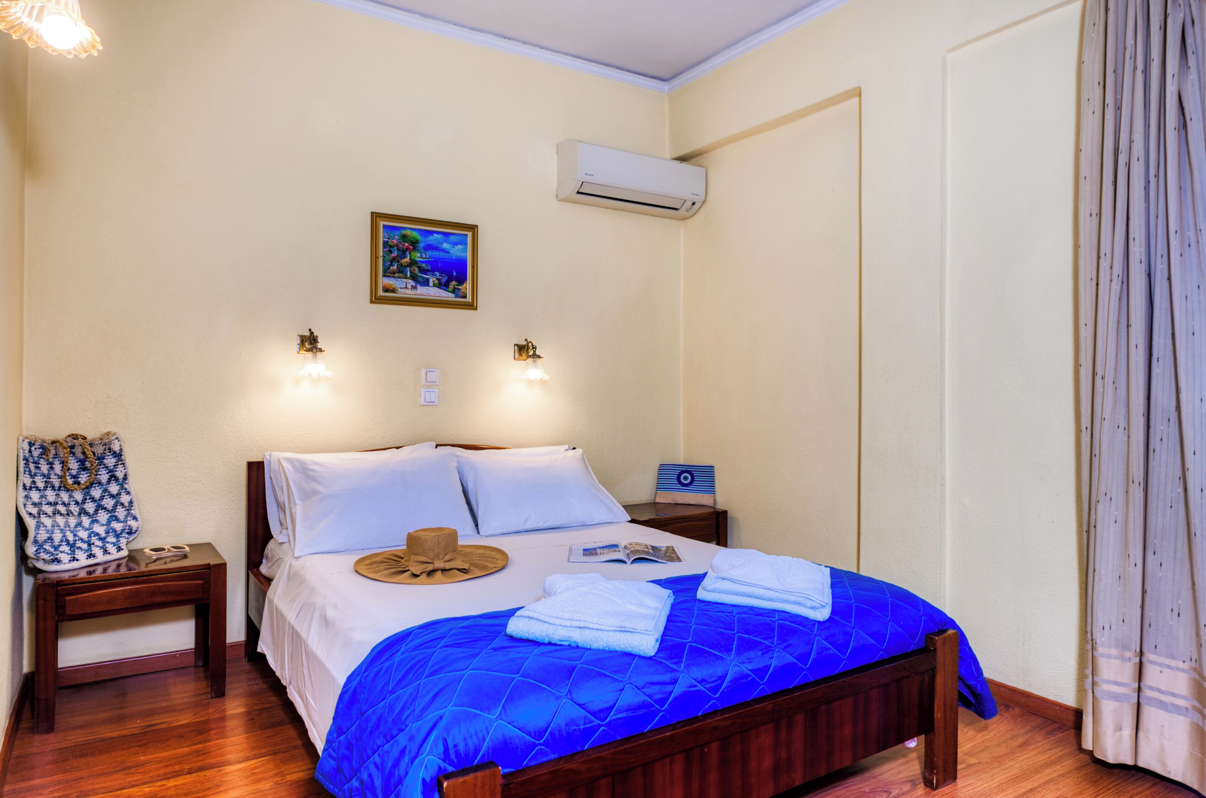 A bedroom with a bed, bedside tables, a wall-mounted air conditioner, and a painting.