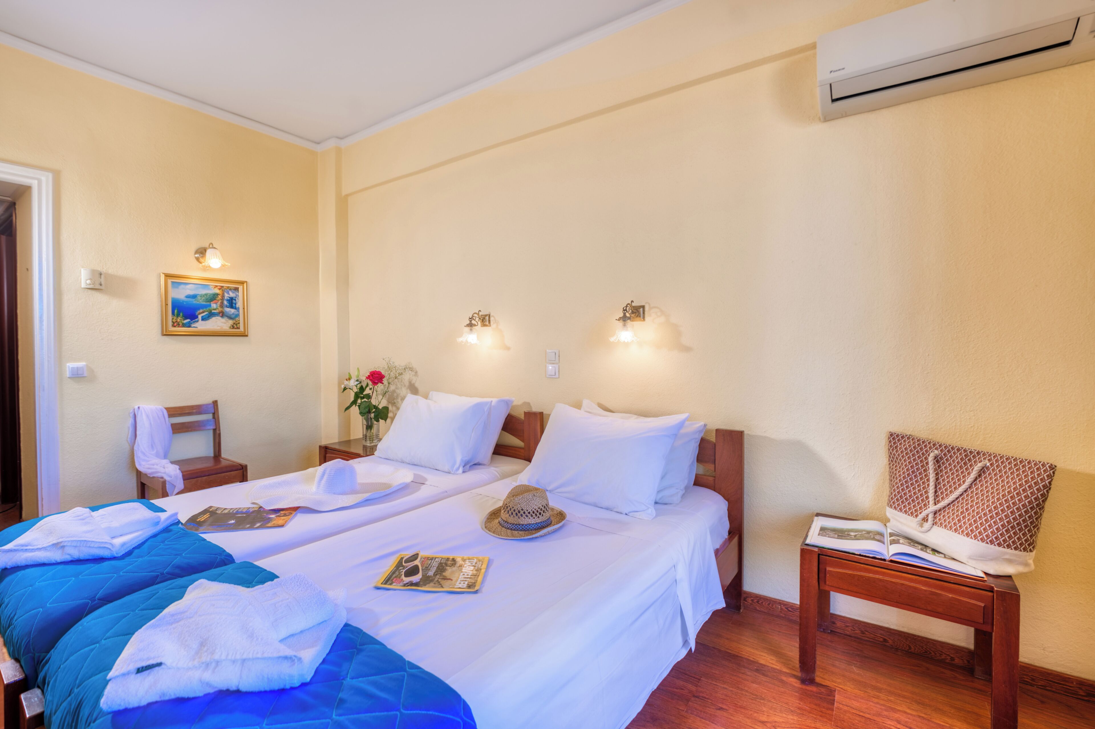 A hotel room with two beds, a wooden nightstand, a chair, a wall-mounted air conditioner, and a painting.