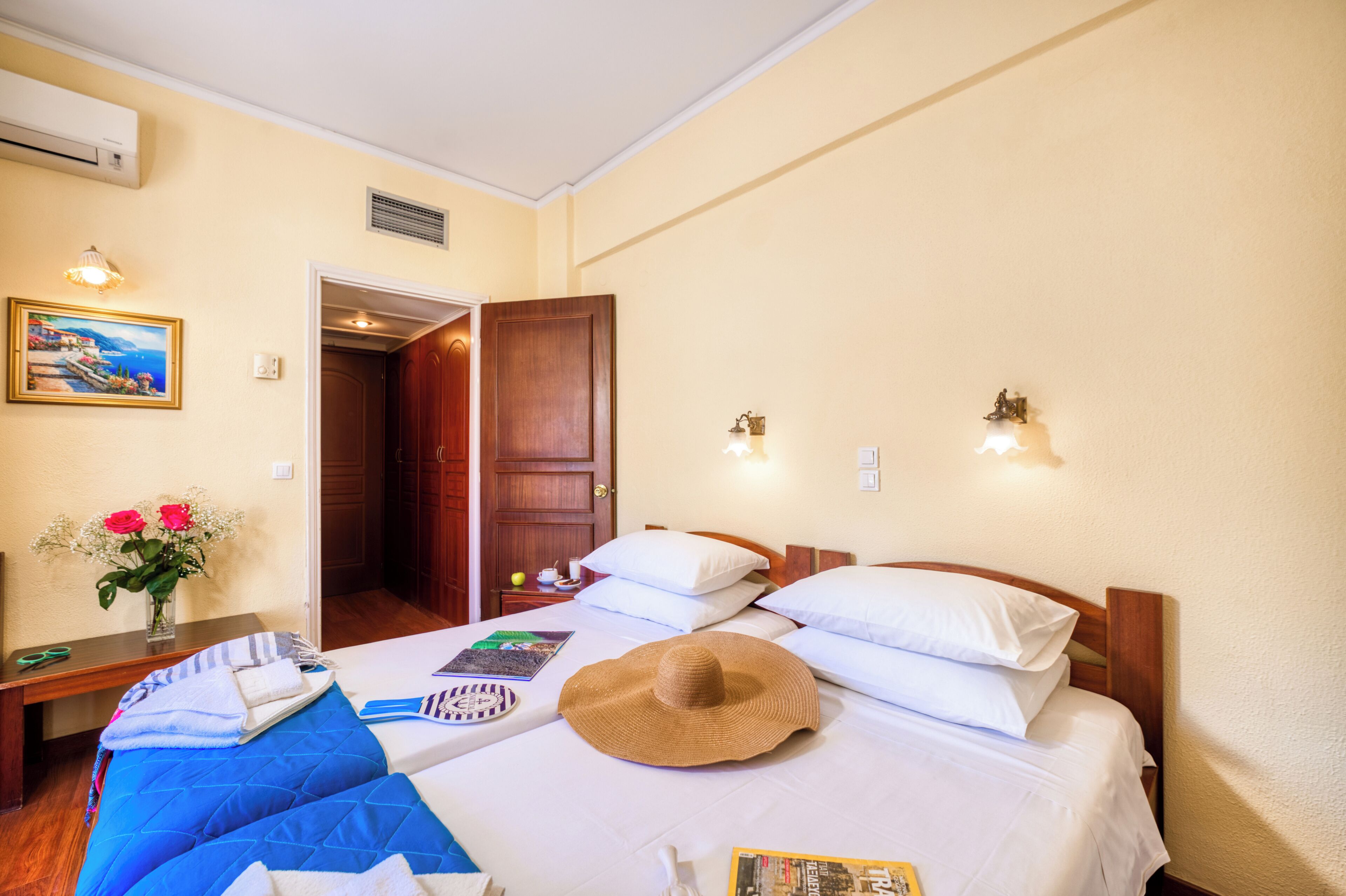 Una habitación de hotel con cama, mesita de noche, lámpara y una puerta que da a otra estancia.