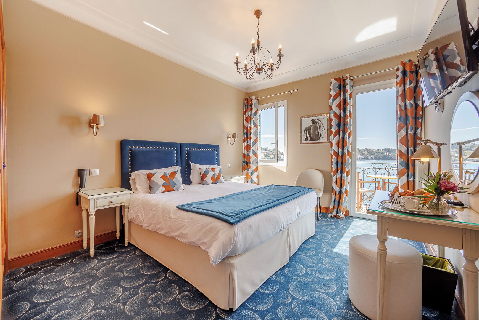 Habitación de hotel con una cama grande, un escritorio con silla, una araña y vista al mar.