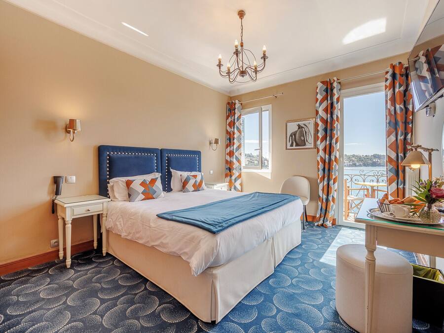 Habitación de hotel con una cama grande, un escritorio con silla, una araña y vista al mar.