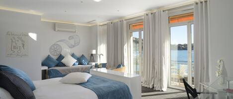Une chambre d’hôtel moderne dotée d’un grand lit, d’un bureau et d’un balcon offrant une vue sur la mer.