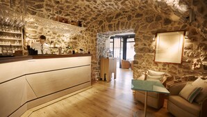 A stone-walled bar area with a wooden counter and shelves of bottles. There is a glass table and a sofa in the foreground. - Welcome Hôtel (Villefranche-sur-Mer)