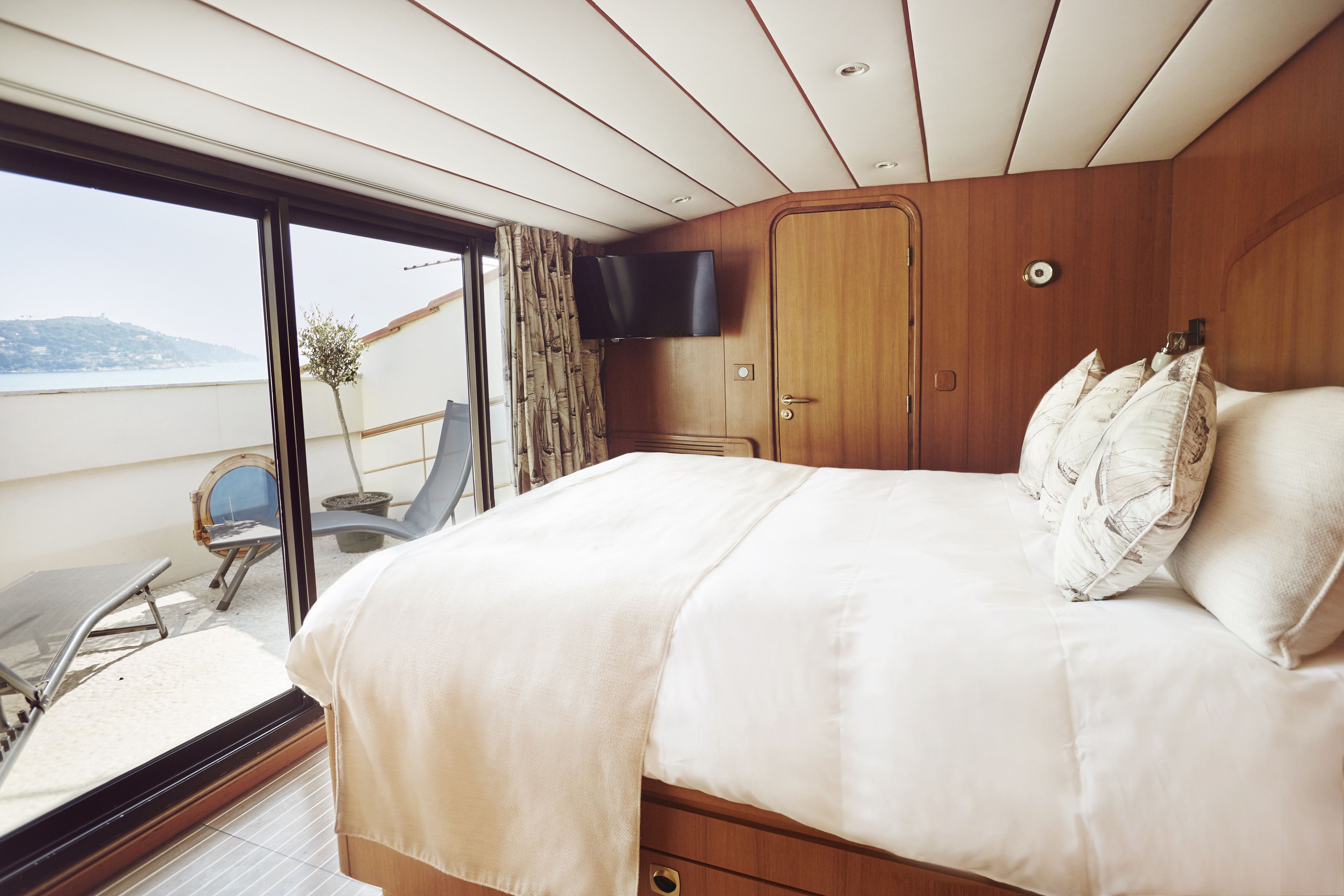 A bedroom with a large bed, a TV mounted on the wall, and a view of the outdoors.