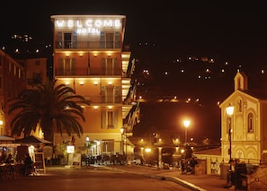 A hotel with a 'WELCOME HOTEL' sign, outdoor seating, and a view of the cityscape.