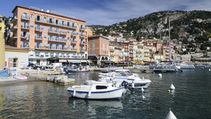 A waterfront hotel with multiple balconies, a marina with boats, and a hillside town in the background. - Welcome Hôtel (Villefranche-sur-Mer)