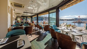 A restaurant with tables and chairs, large windows, and a view of the water. - Welcome Hôtel (Villefranche-sur-Mer)
