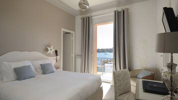 Ein Hotelzimmer mit Bett, einem Sessel, einem Tisch mit Lampe und Meerblick durch das Fenster.