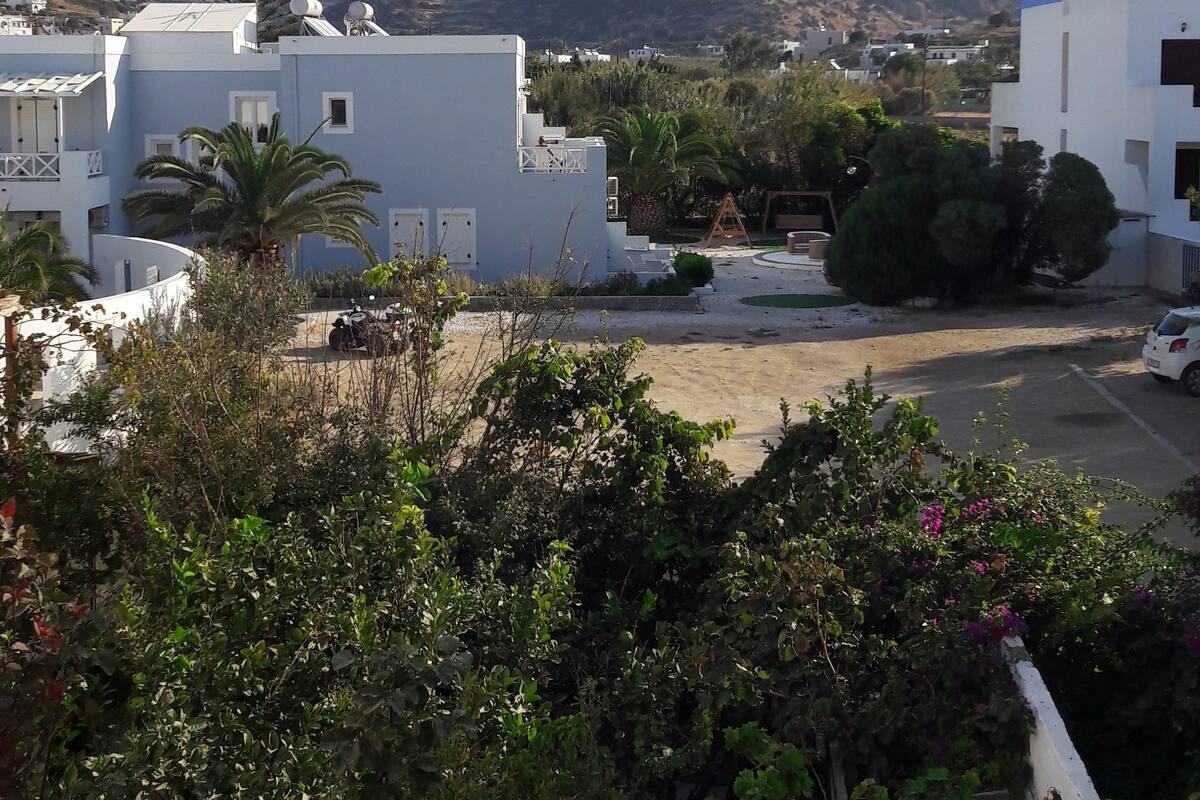 A residential area with white buildings, a clear sky, and a hilly landscape in the background.