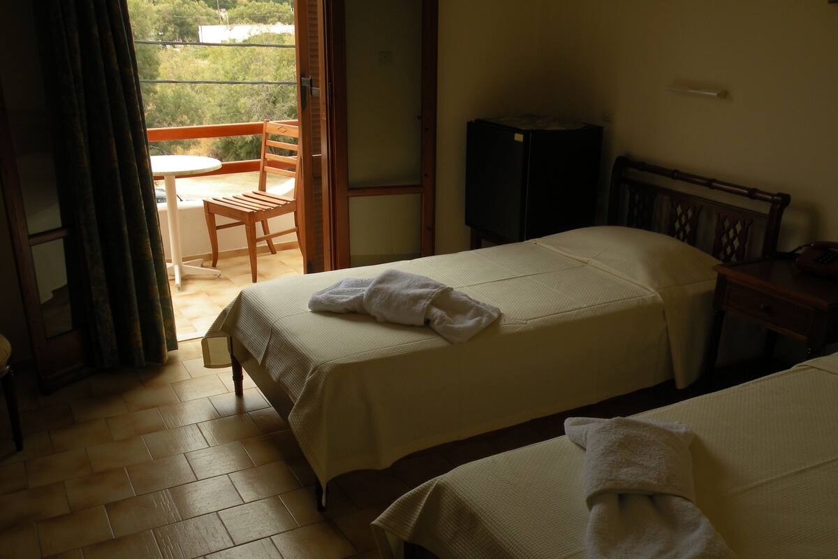 A hotel room with two beds, a balcony, a television, and a wooden chair.