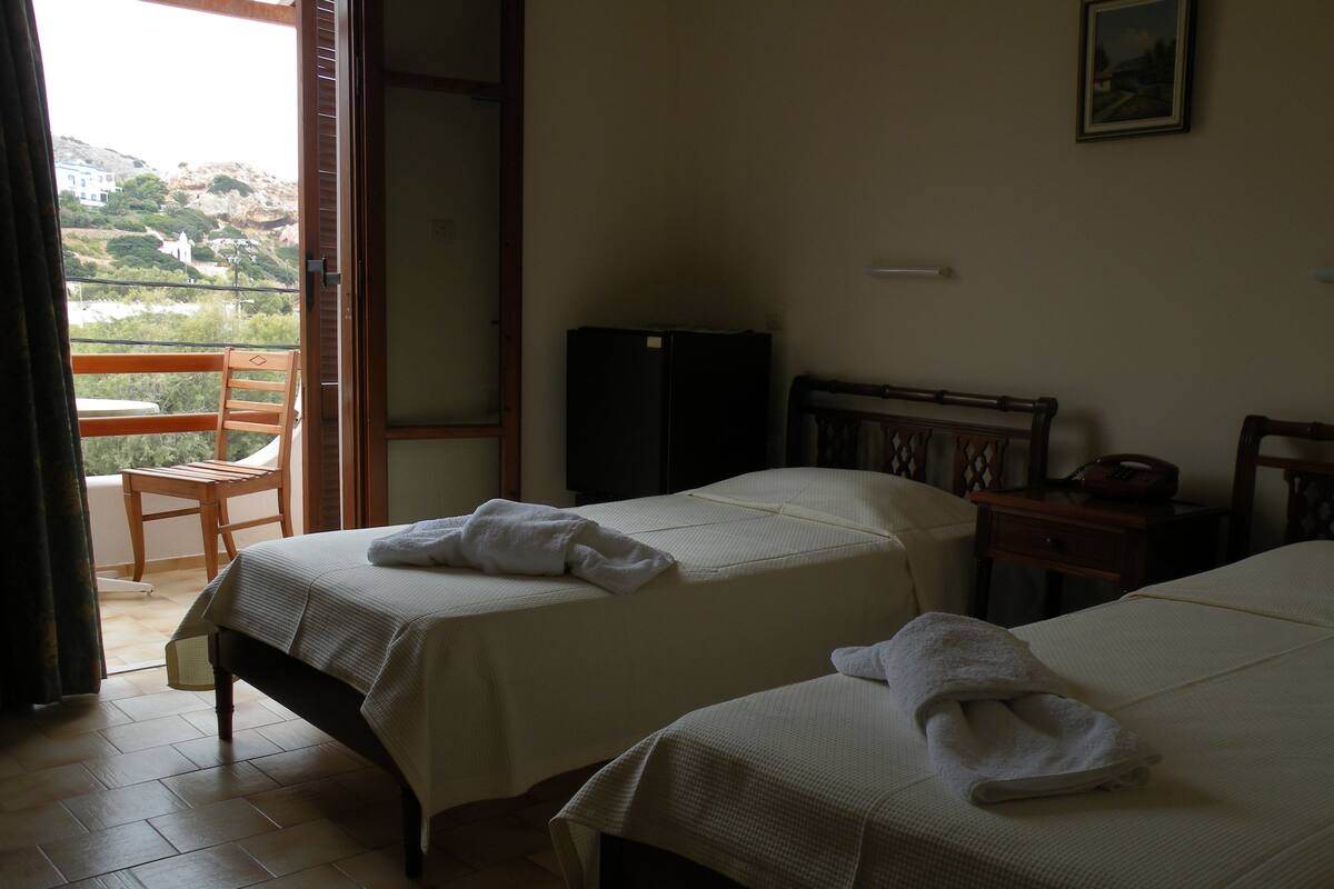 A hotel room with two beds, a chair, a desk, and a television.