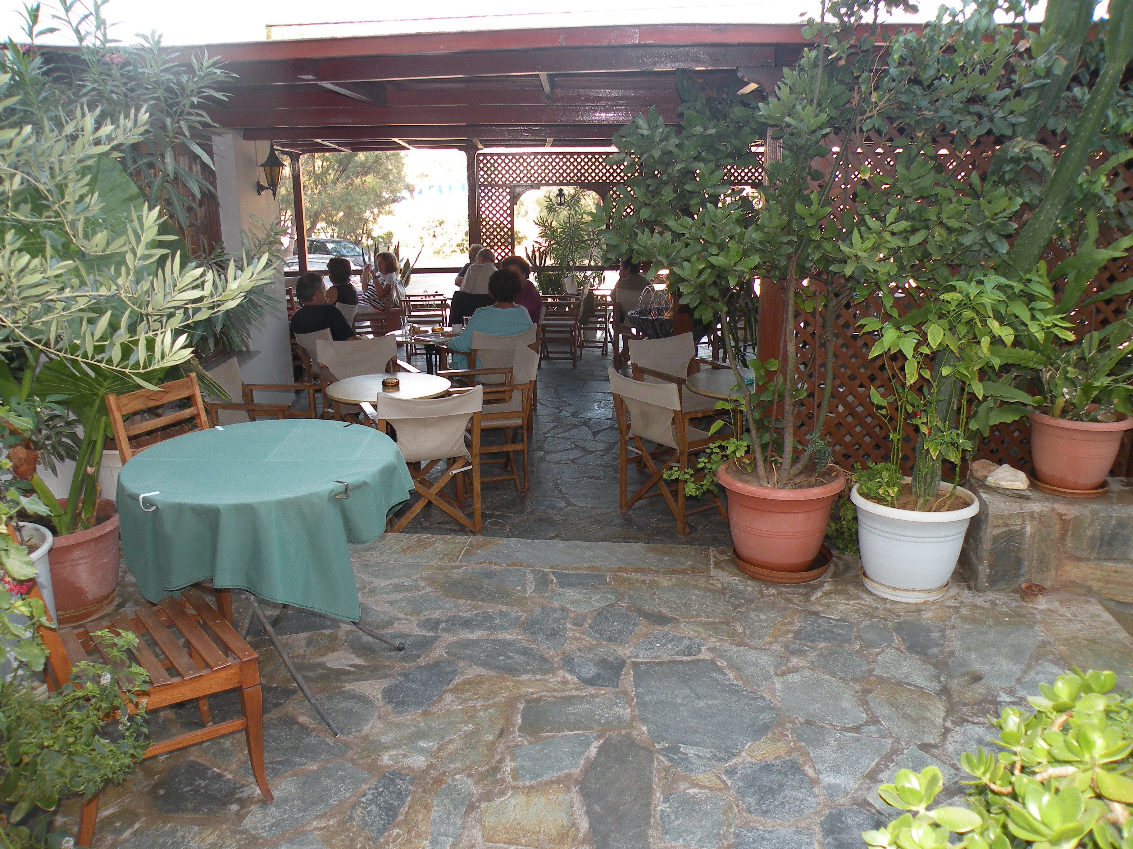 An outdoor patio area with stone flooring, wooden tables and chairs, and potted plants.
