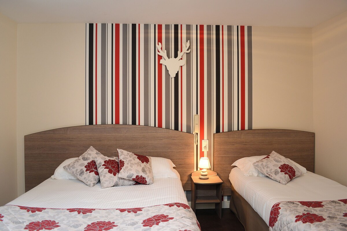 A hotel room with two beds, striped wallpaper, a deer head decoration, and a nightstand with a lamp.