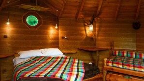 A cozy cabin with a wooden interior, a circular skylight, a bed with a colorful blanket, and a small table with a lantern. - Hôtel Andreinia (Esterencuby)