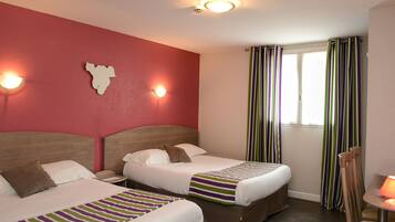 A hotel room with two beds, a red accent wall, a window with striped curtains, and a small table with a lamp.