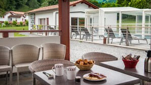 A terrace with wicker chairs, a table with breakfast items, and a view of a lake and buildings in the background. - Hôtel Andreinia (Esterencuby)