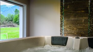 A hot tub with a view of a green landscape through a window. - Hôtel Andreinia (Esterencuby)
