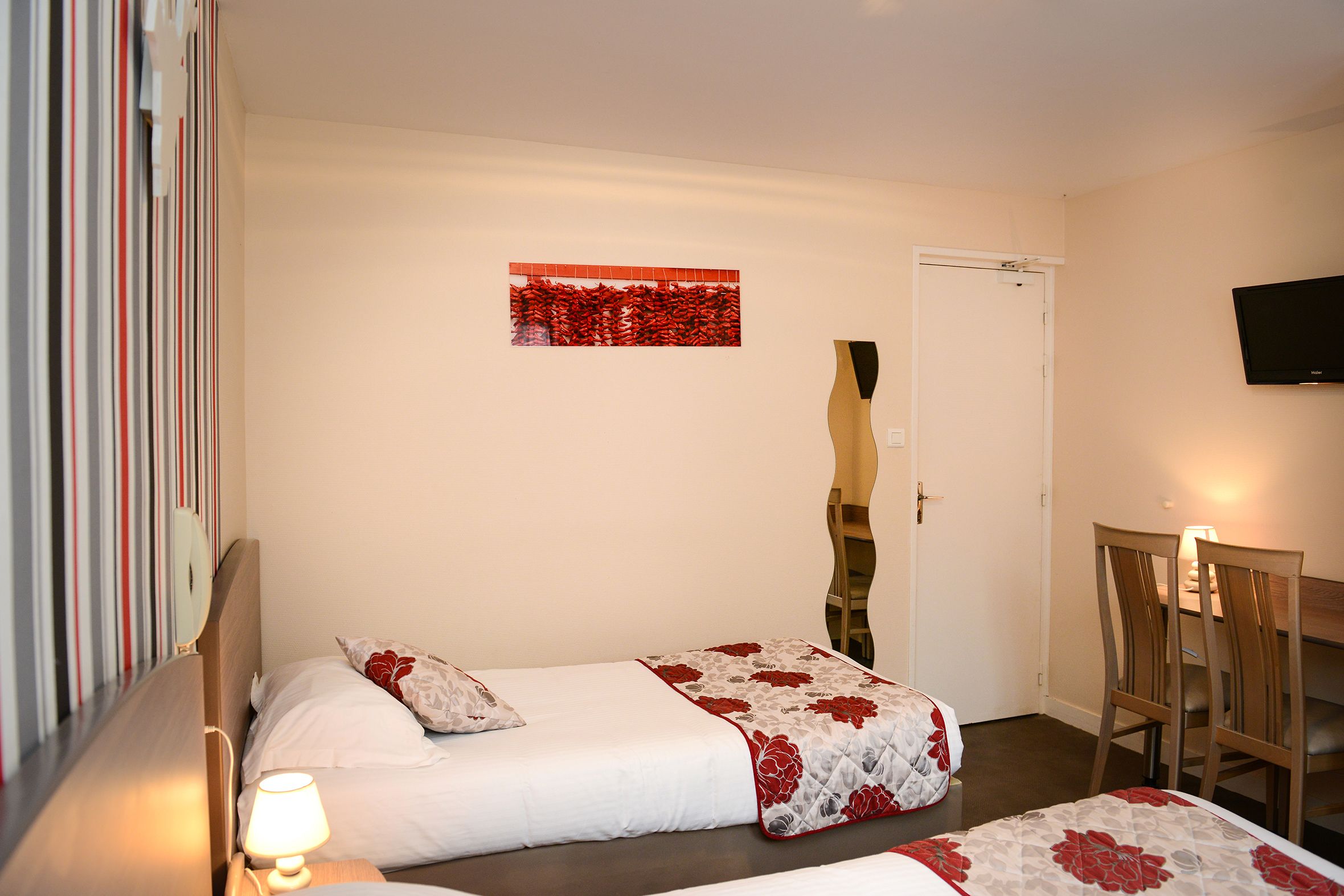 A hotel room with two beds, a television, and a dining area with chairs and a table.