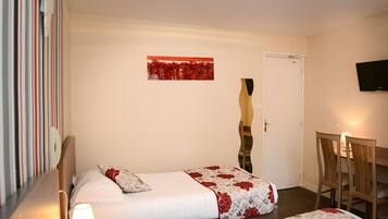 A hotel room with two beds, a television, and a dining area with chairs and a table.