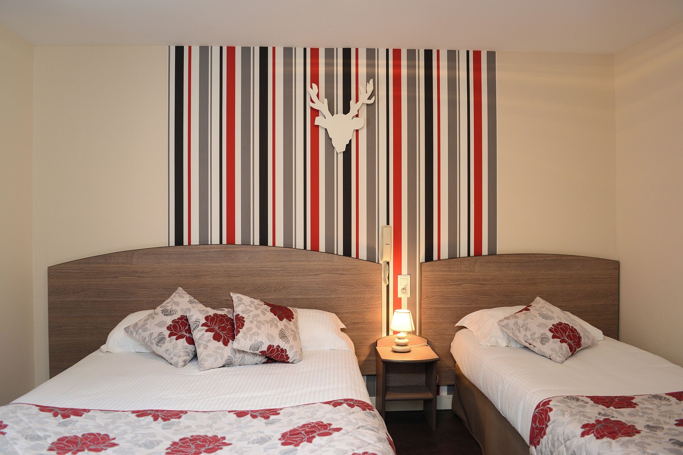 A double bed with floral-patterned bedding, a headboard with a deer head decoration, and a striped wall with vertical stripes in red, black, and white.