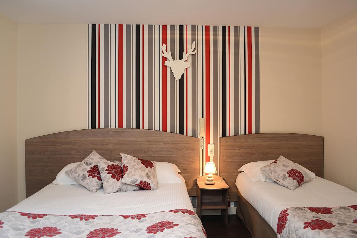 A hotel room with two beds, striped wallpaper, a deer head decoration, and a nightstand with a lamp.