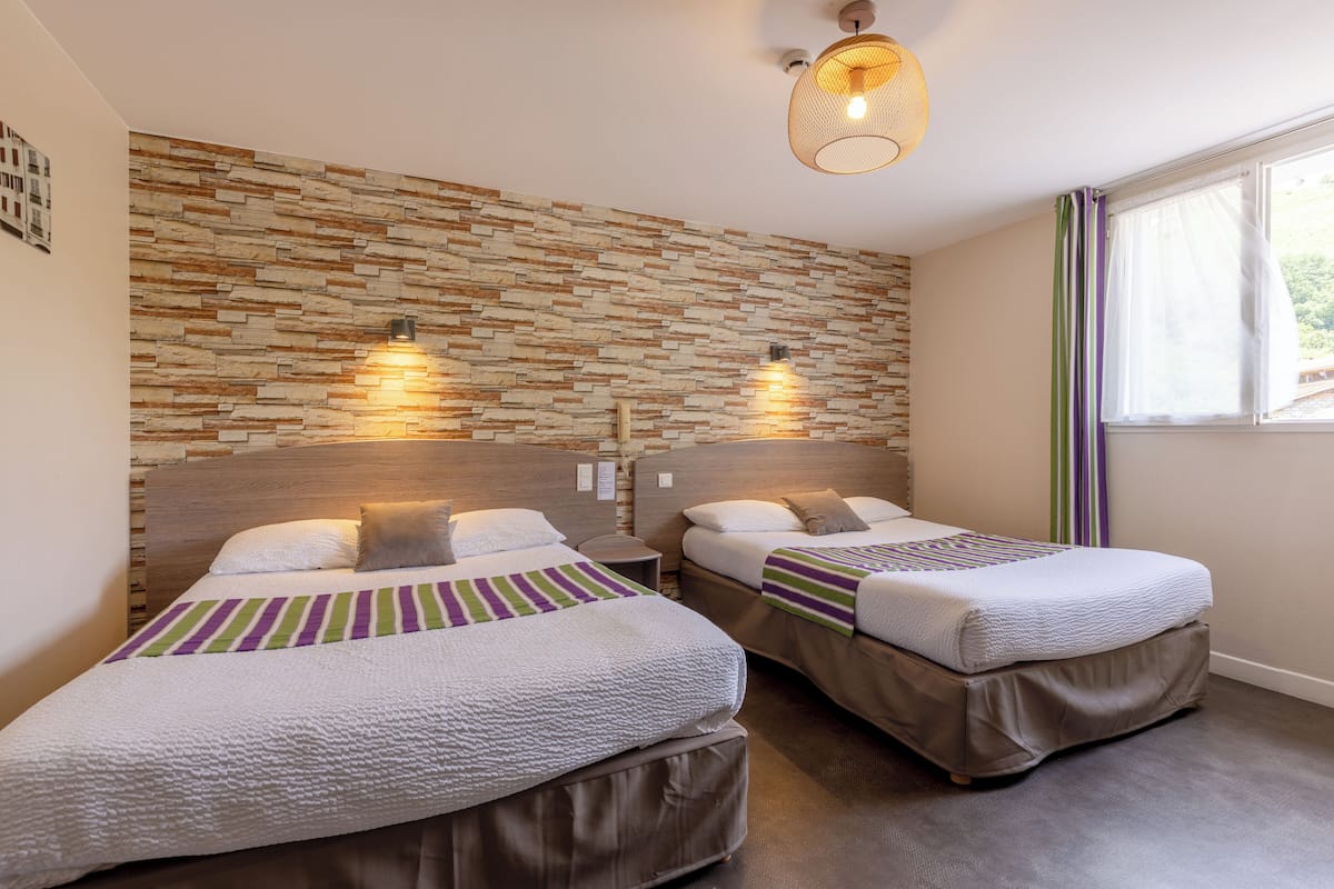 A hotel room with two beds, a stone wall, and a window with curtains.