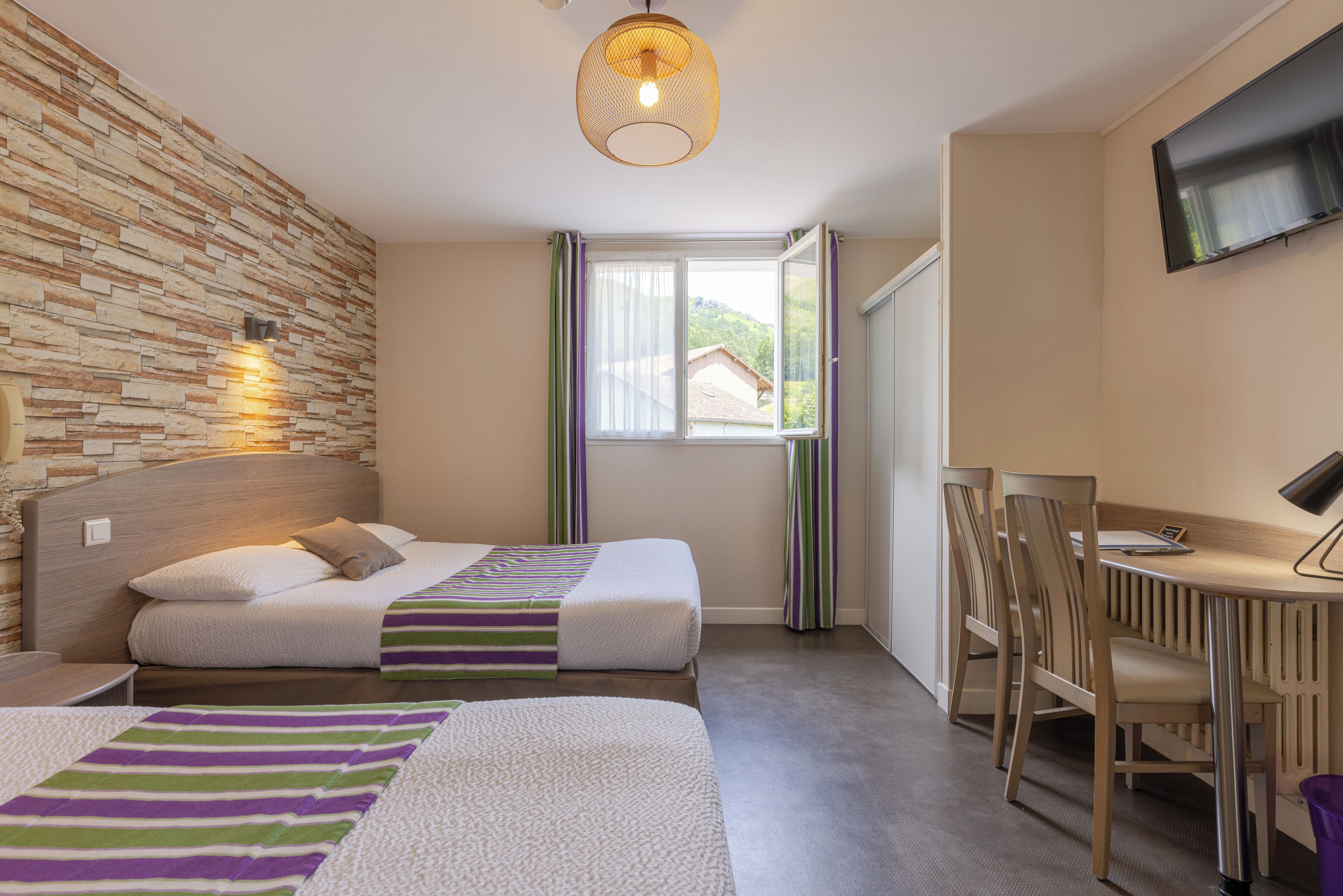 Quarto de hotel com duas camas, uma escrivaninha, uma cadeira, uma televisão e uma janela com cortinas.