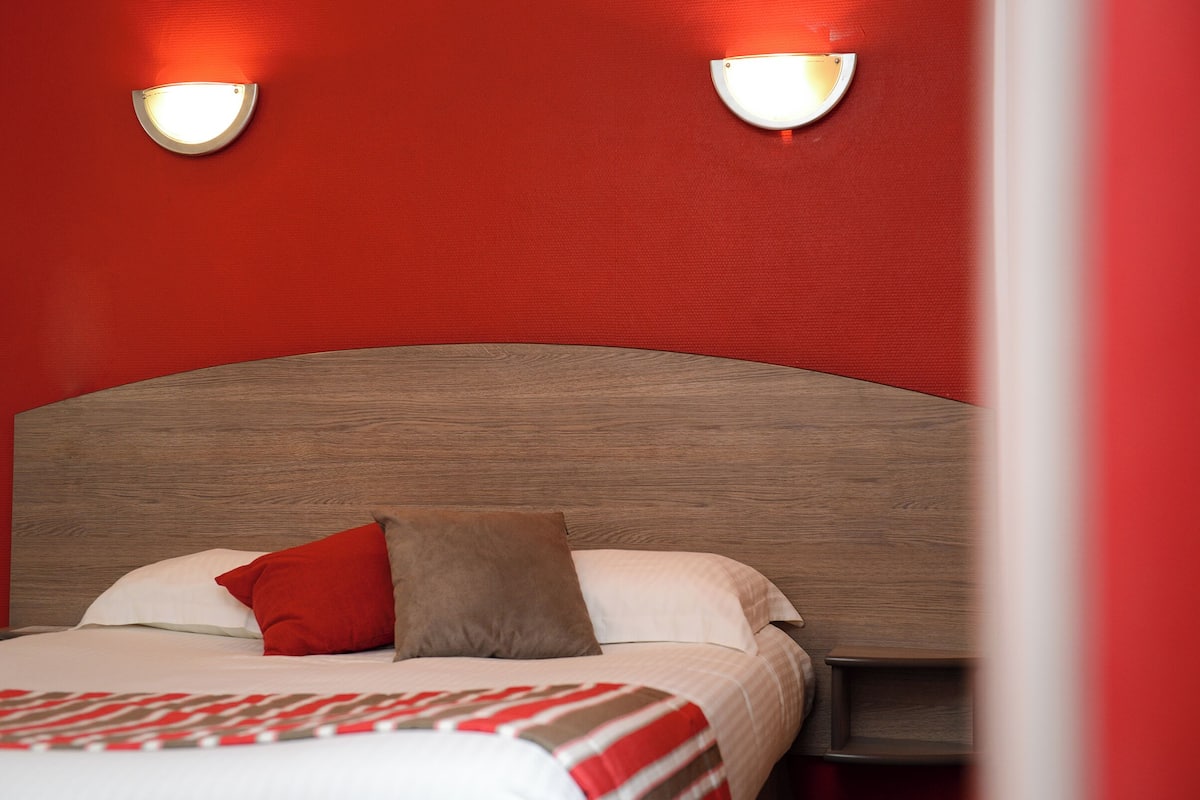 A bed with a wooden headboard, two wall-mounted lights, and a red and white striped blanket.