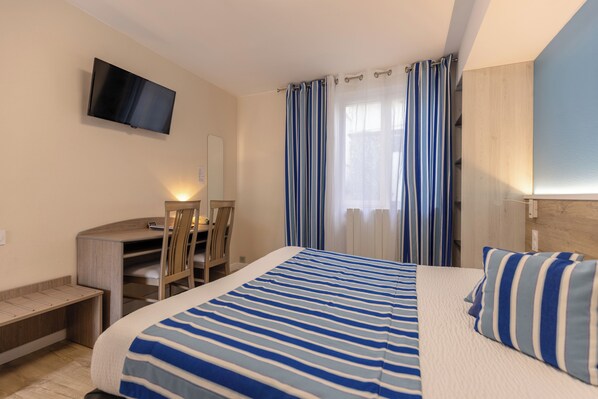 A hotel room with a bed, a desk, a chair, a television, and curtains.