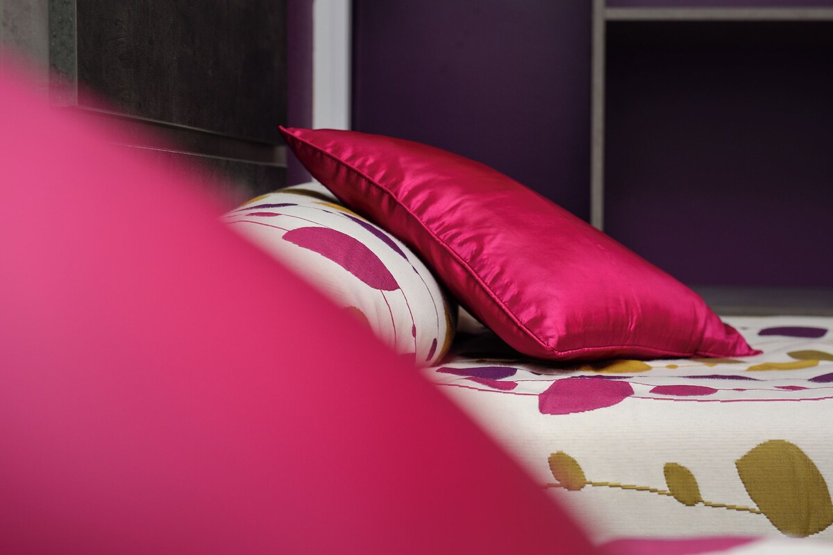 A bed with a floral-patterned bedspread and two pillows, one white and one pink.