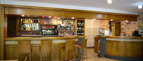 A bar area with wooden bar stools, a counter with various bottles, and a stone wall in the background.