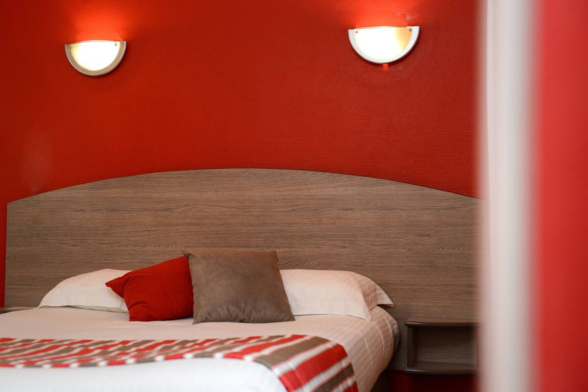 A bed with a wooden headboard, two wall-mounted lights, and a red and white striped blanket.