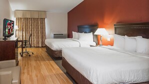 Habitación de hotel con dos camas, un escritorio con televisor, una silla, una lámpara y una ventana con cortinas.