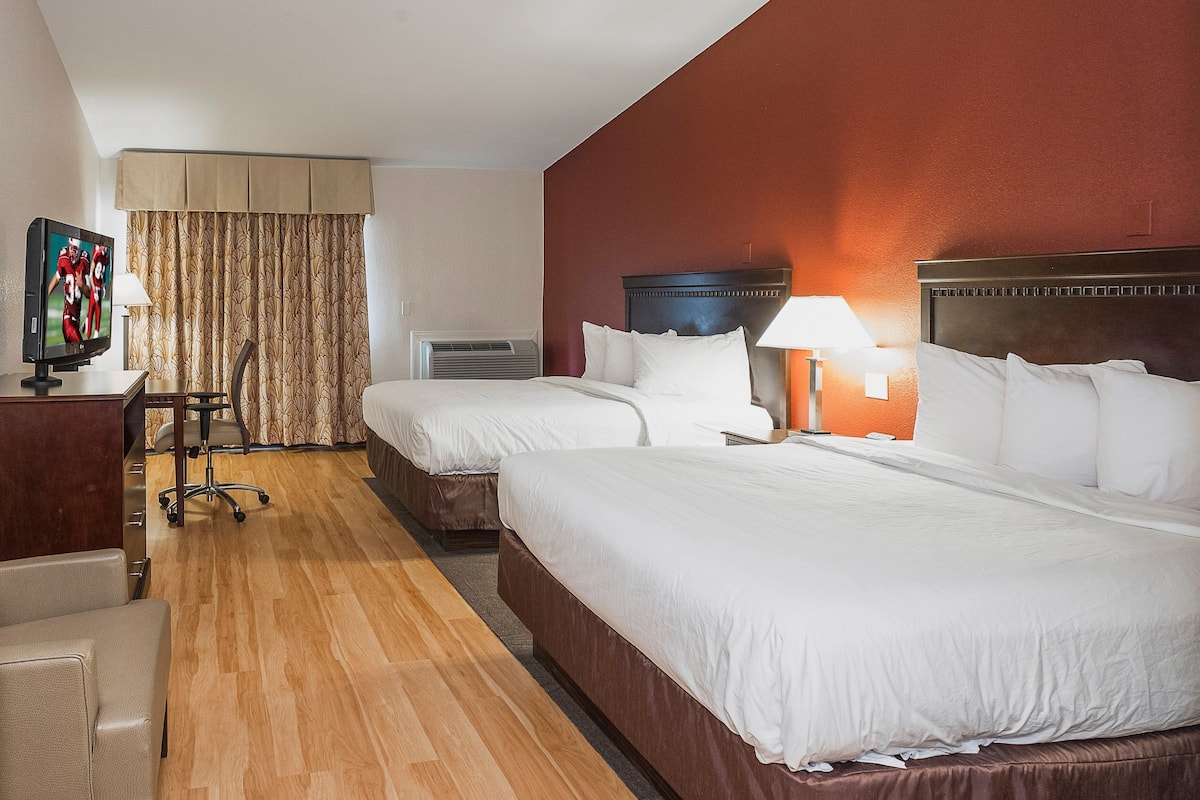 Una habitación de hotel con dos camas, televisión, escritorio y silla.