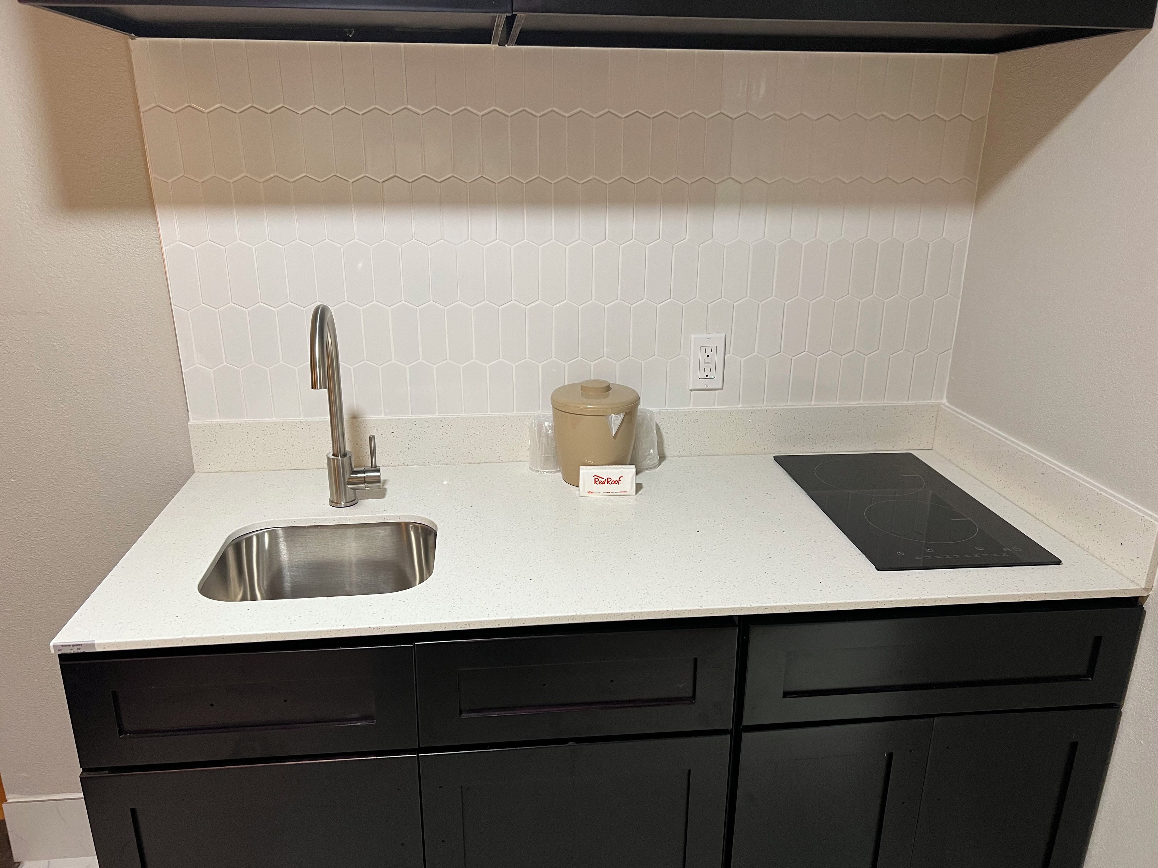 Una cocina con un lavamanos de acero inoxidable, una cocina de inducción negra y una olla de cocción lenta color beige.