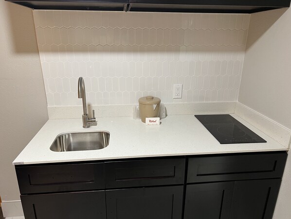 Una cocina con un lavamanos de acero inoxidable, una placa de inducción negra y una cocedora de cerámica color beige.