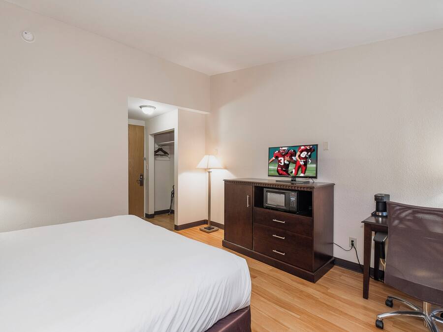 Habitación de hotel con cama, escritorio con computadora, silla, lámpara y televisor.