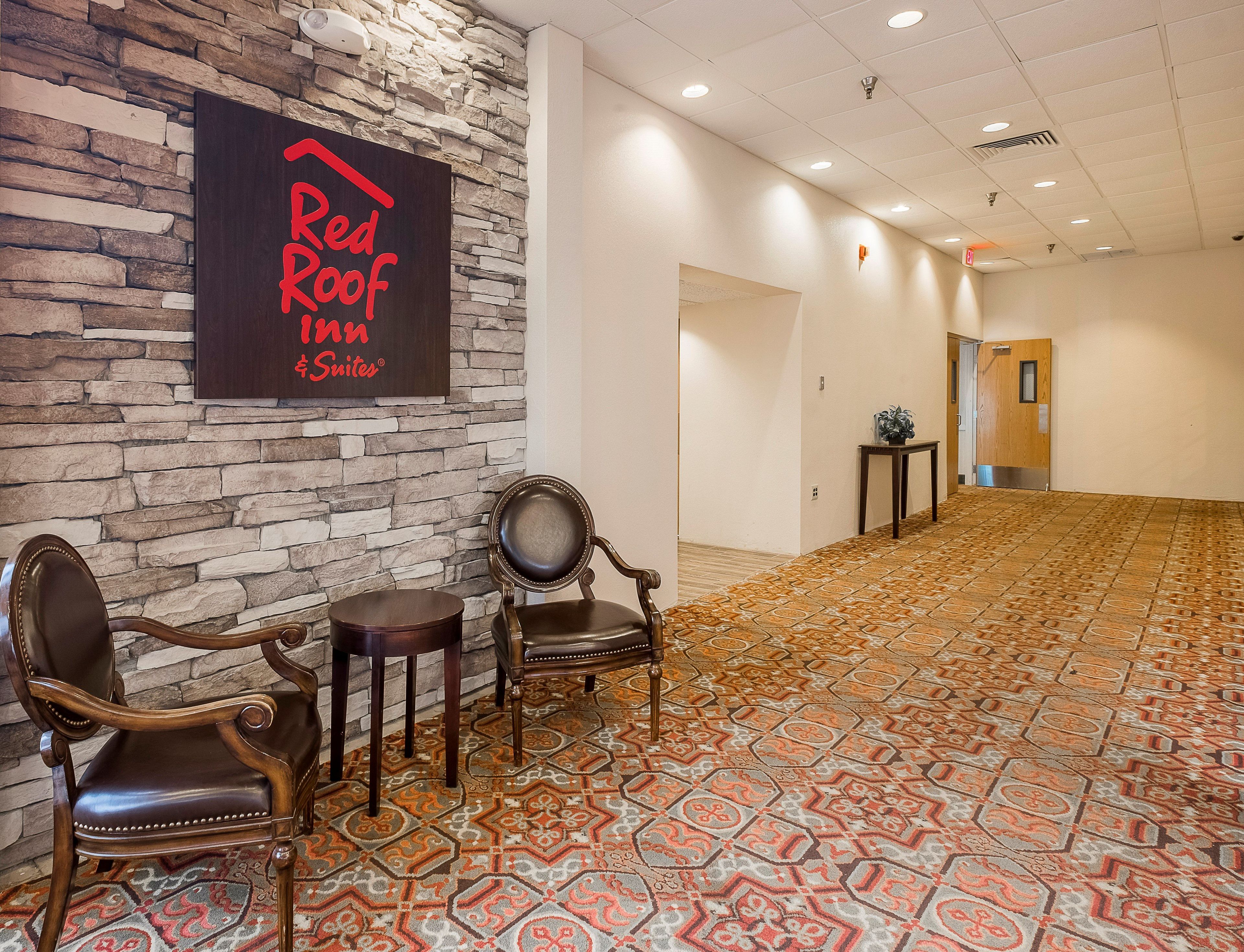 Lobby do Red Roof Inn com paredes de pedra, carpete estampado e duas poltronas de couro.