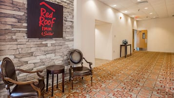 Lobby do Red Roof Inn com paredes de pedra, carpete estampado e duas poltronas de couro.